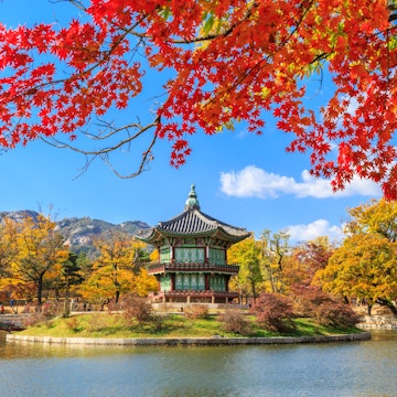 Pavilion in the pond at Gyeongbokgung Palace with autumn foliage and mountain at background while crimson maple tree in the upper foreground, Seoul, South Korea, 2014