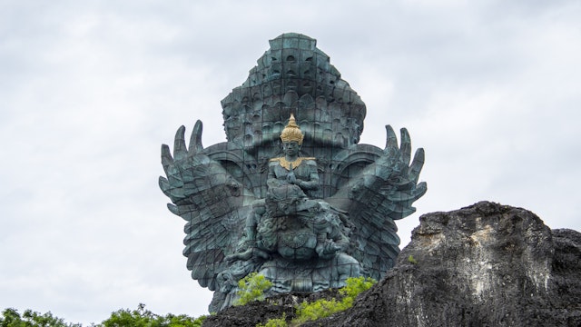 Bali, Indonesia - January 2019 - Garuda Wisnu Kencana statue towers above the rocky cliffs. Located in Garuda Wisnu Kencana Cultural Park it was designed by Nyoman Nuarta and inaugurated in September 2018, 28 years since its inception. Made of brass and copper sheeting and a wingspan of 64m ,the total height of the monument is 121 m (397ft), making it Indonesia's tallest and one of the world's largest.