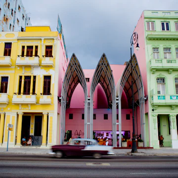 Vintage car passing modern bar nestled between dilapidated Art Nouveau buildings along the Av de Malecon.