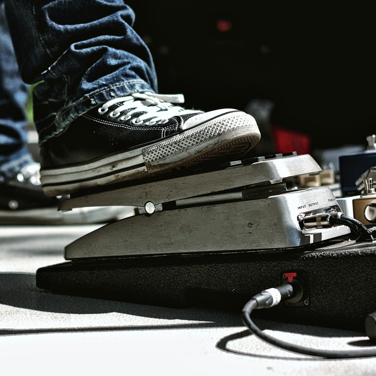 Guitarist with skinny jeans, on outdoor stage playing live music standing with his pedalboard full of stomboxes and guitar pedals at a concert.