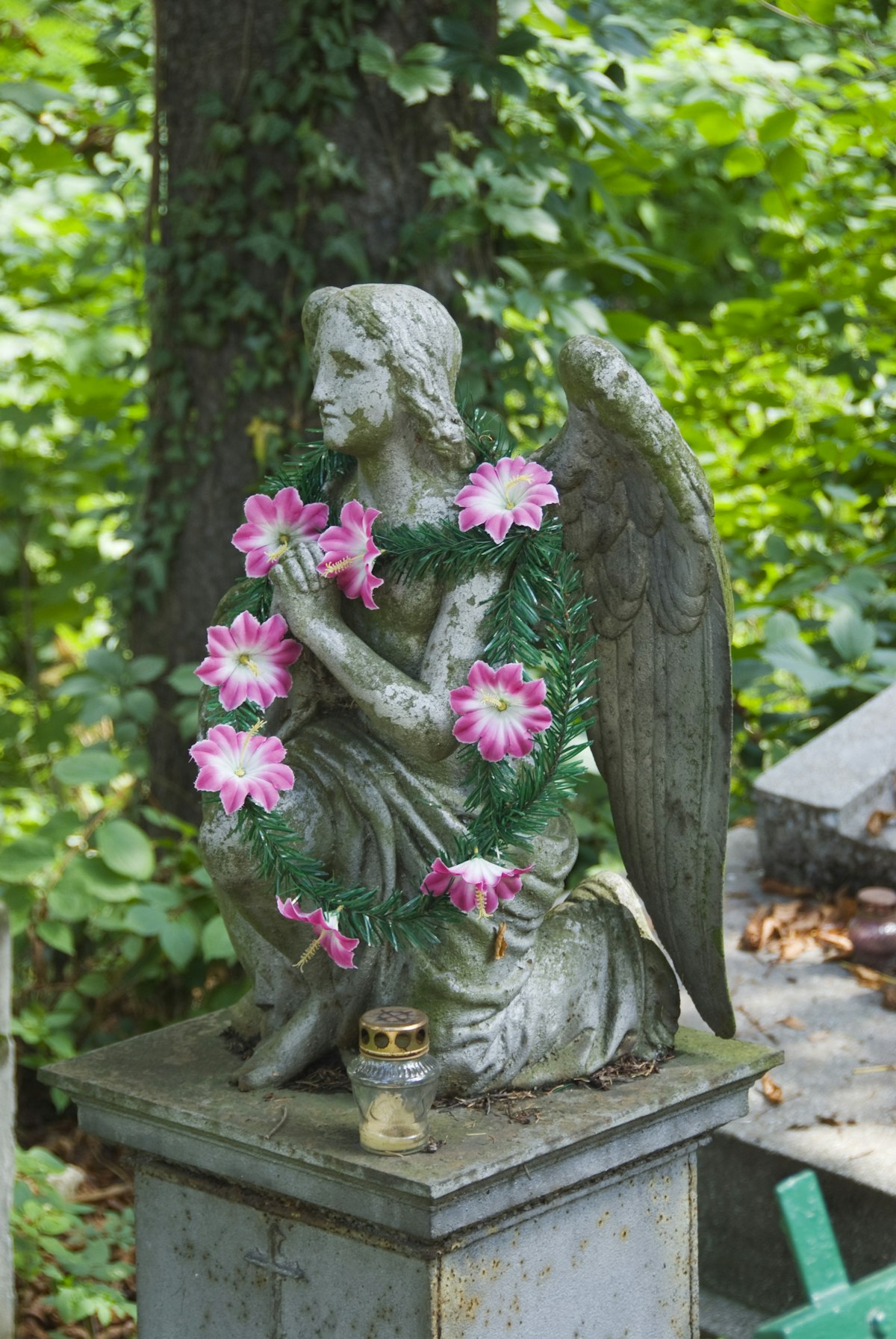 Artifical flowers decorating small winged angel statue on grave at Lychakivske Cemetery.