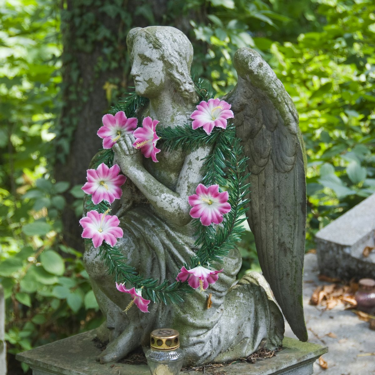Artifical flowers decorating small winged angel statue on grave at Lychakivske Cemetery.