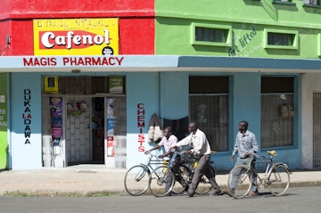 Men pushing bikes past pharmacy on corner.