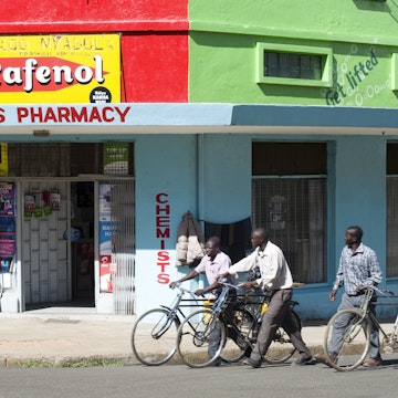 Men pushing bikes past pharmacy on corner.