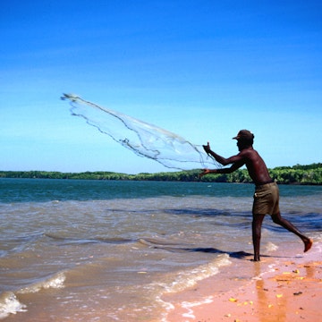 Man casting fishing net on beach.