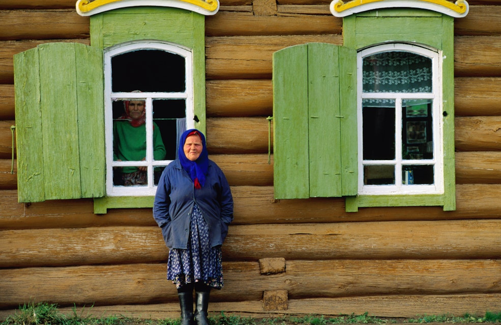 Woman in front of log house.