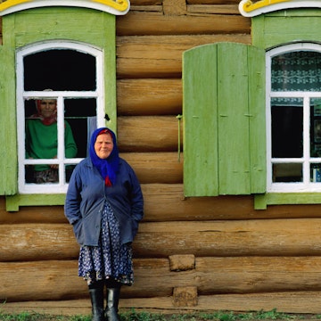 Woman in front of log house.