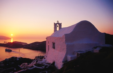 Whitewashed hilltop church and Aegean Sea at sunset.