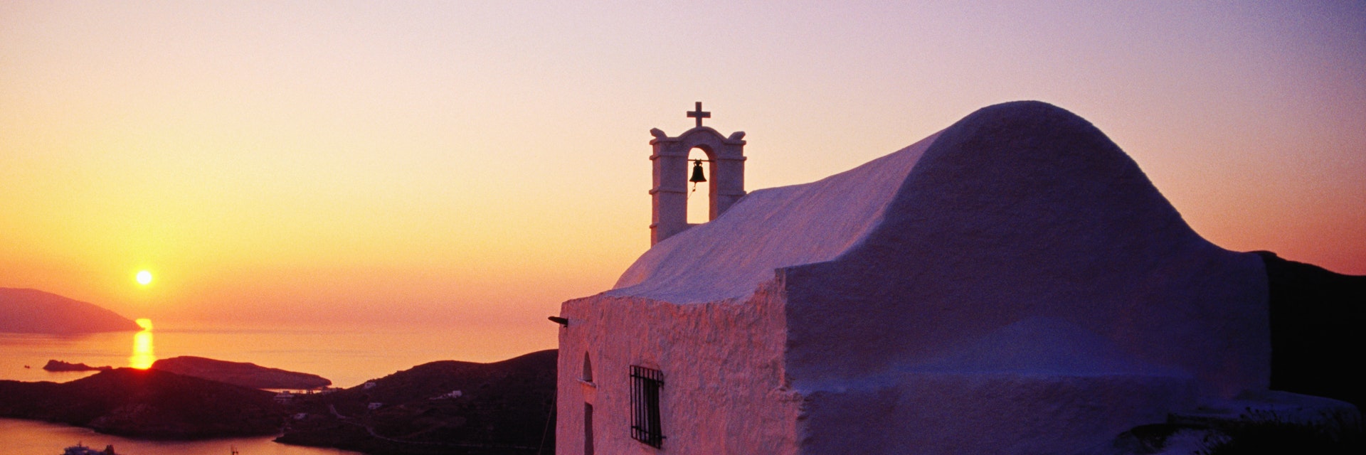 Whitewashed hilltop church and Aegean Sea at sunset.