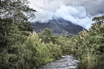Stream running through forest with Arenal Volcano in background.