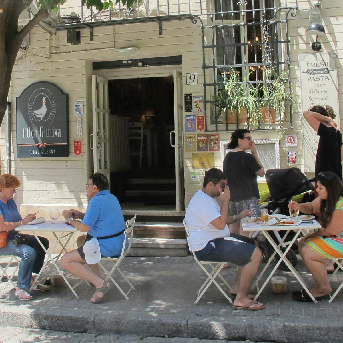 L’Oca Giuliva restaurant people sitting at tables on pavement.