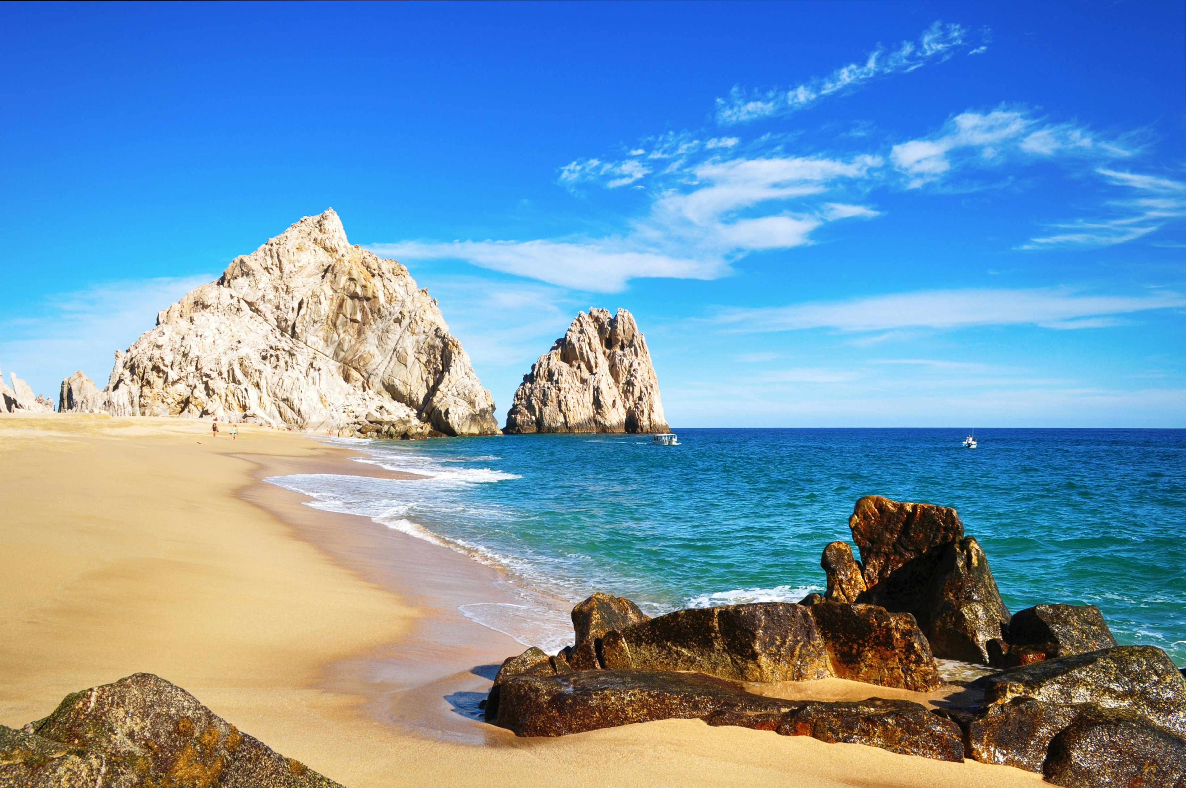 A white-sand beach with rocks in the distance on a sunny day