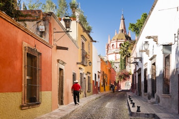 Man walking down a cobblestone street with chuch dome in distance.