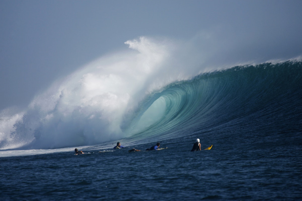 Surfers look on as a large wave rolls through at G-Land, Java, Indonesia.