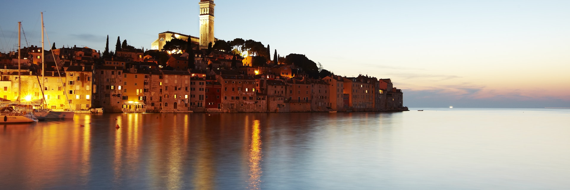 View of port town and tower of Saint Euphemia's basilica at dusk.