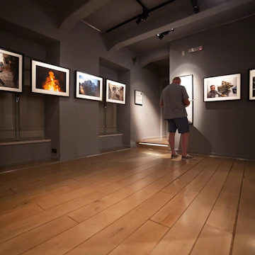 DUBROVNIK, CROATIA - MAY 26, 2014: Tourist looking at photos in the War photo limited gallery. There is 350m2 of exhibition space on two floors. ; Shutterstock ID 215780338; Your name (First / Last): Josh Vogel; GL account no.: 56530; Netsuite department name: Online Design; Full Product or Project name including edition: Digital Content/Sights