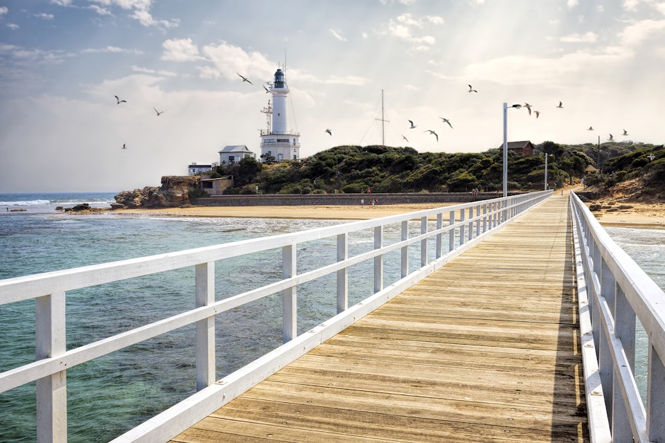 View of Point Lonsdale Lighthouse and jetty with seagulls in sky, Bellarine Peninsula, Victoria, Australia