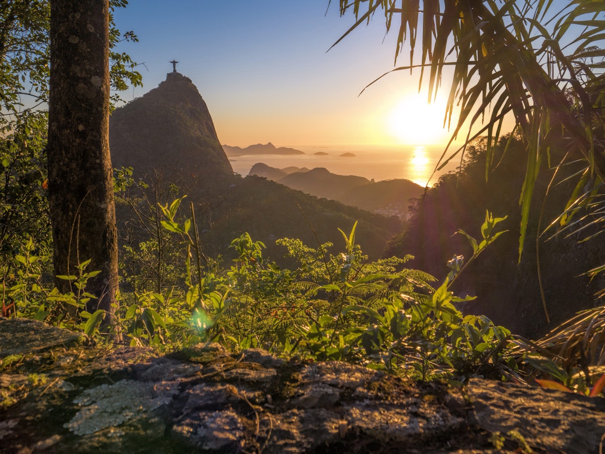 The sunset with Christ The Redeemer on the Corcovado Hill viewed from Paineiras Road at Tijuca Forest with the Atlantic Ocean in the distance.