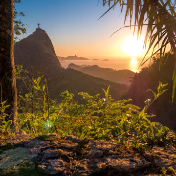 The sunset with Christ The Redeemer on the Corcovado Hill viewed from Paineiras Road at Tijuca Forest with the Atlantic Ocean in the distance.