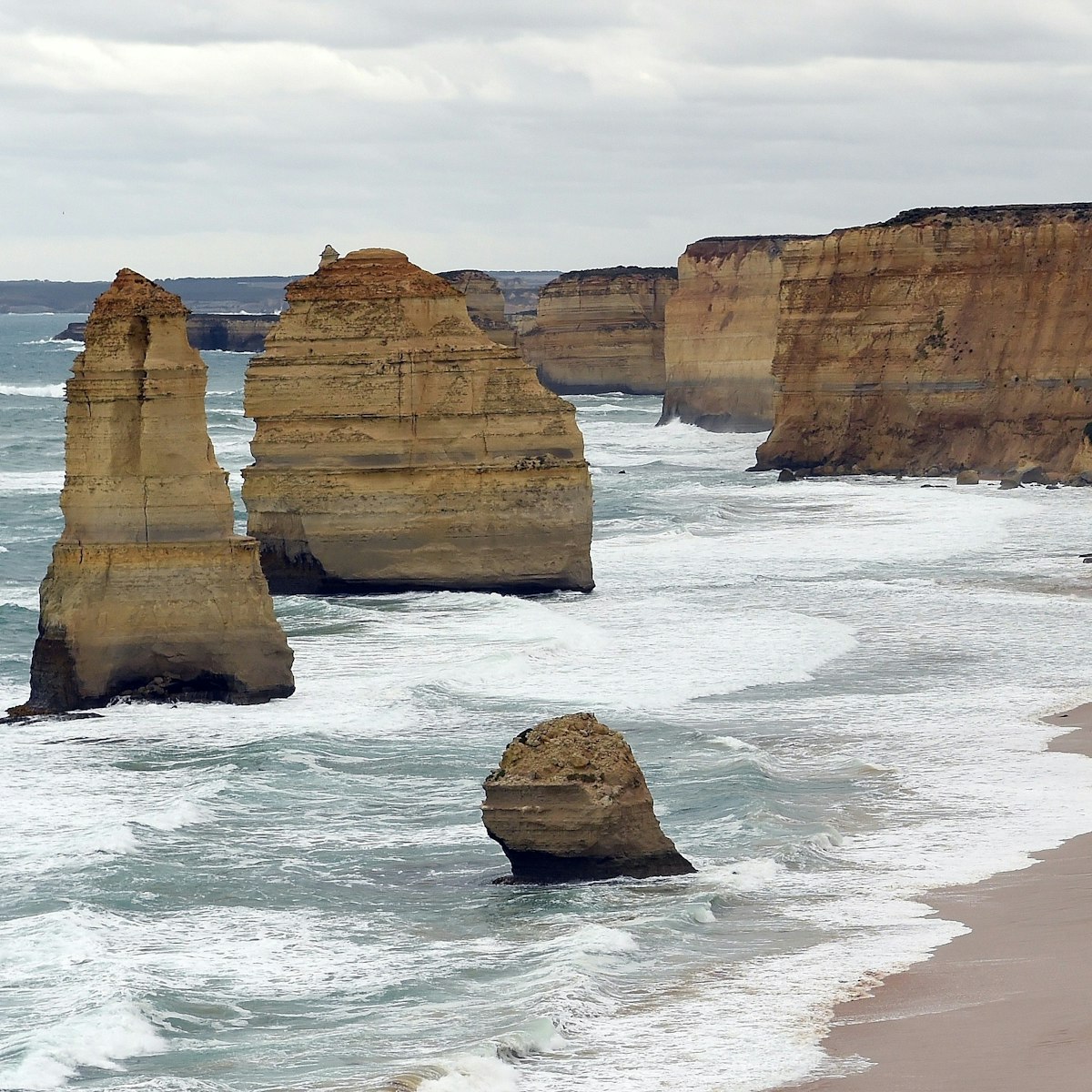 In this photo taken on March 24, 2015, waves crash into the base of natural limestone structures known as the Twelve Apostles off the shore of the Port Campbell National Park, by the Great Ocean road in Victoria. The close proximity of the collection of limestone stacks to one another has made the site a popular tourist attraction.  AFP PHOTO / INDRANIL MUKHERJEE        (Photo credit should read INDRANIL MUKHERJEE/AFP/Getty Images)