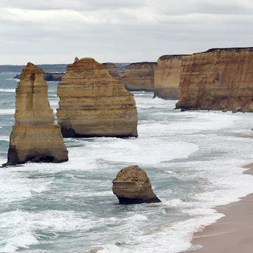 In this photo taken on March 24, 2015, waves crash into the base of natural limestone structures known as the Twelve Apostles off the shore of the Port Campbell National Park, by the Great Ocean road in Victoria. The close proximity of the collection of limestone stacks to one another has made the site a popular tourist attraction. AFP PHOTO / INDRANIL MUKHERJEE (Photo credit should read INDRANIL MUKHERJEE/AFP/Getty Images)
