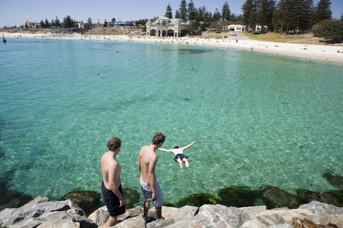 Young men jumping off the rocks at Cottesloe Beach with Indiana Teahouse in the background.