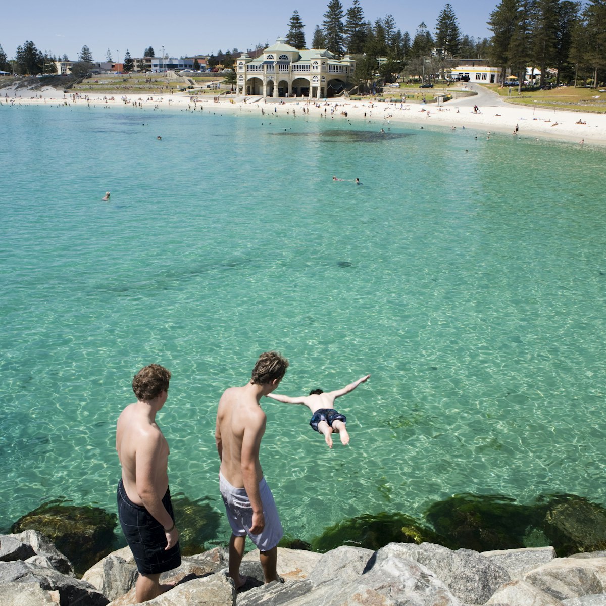 Young men jumping off the rocks at Cottesloe Beach with Indiana Teahouse in the background.