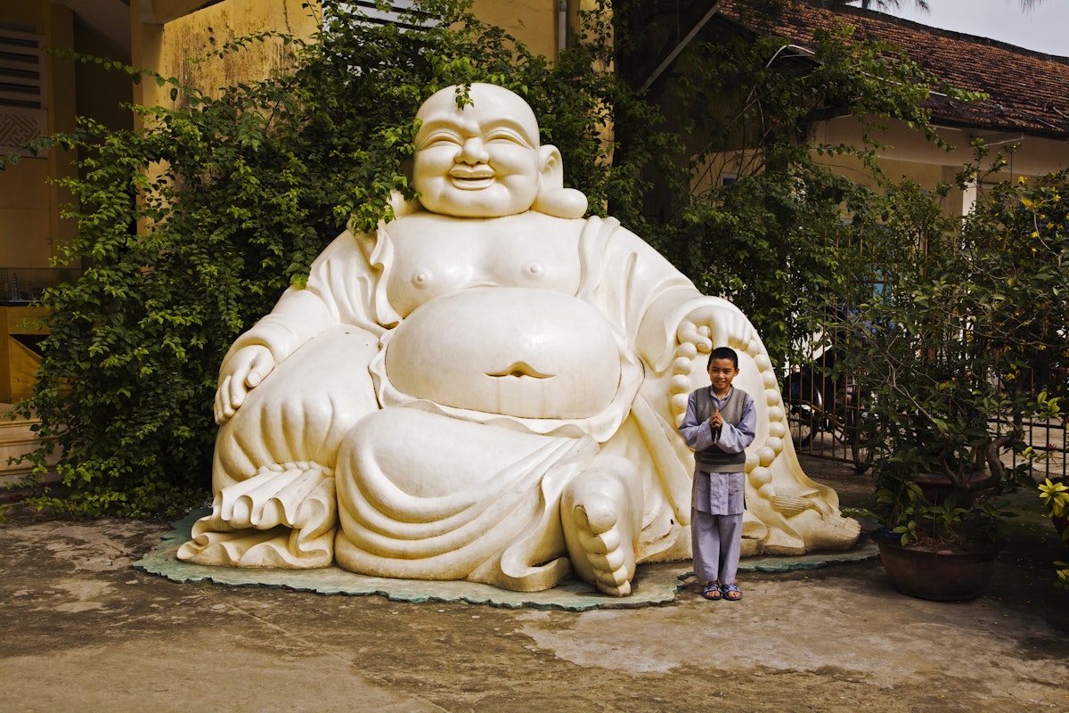 Boy making prayer gesture by giant Buddha outside Phap Lam Pagoda.