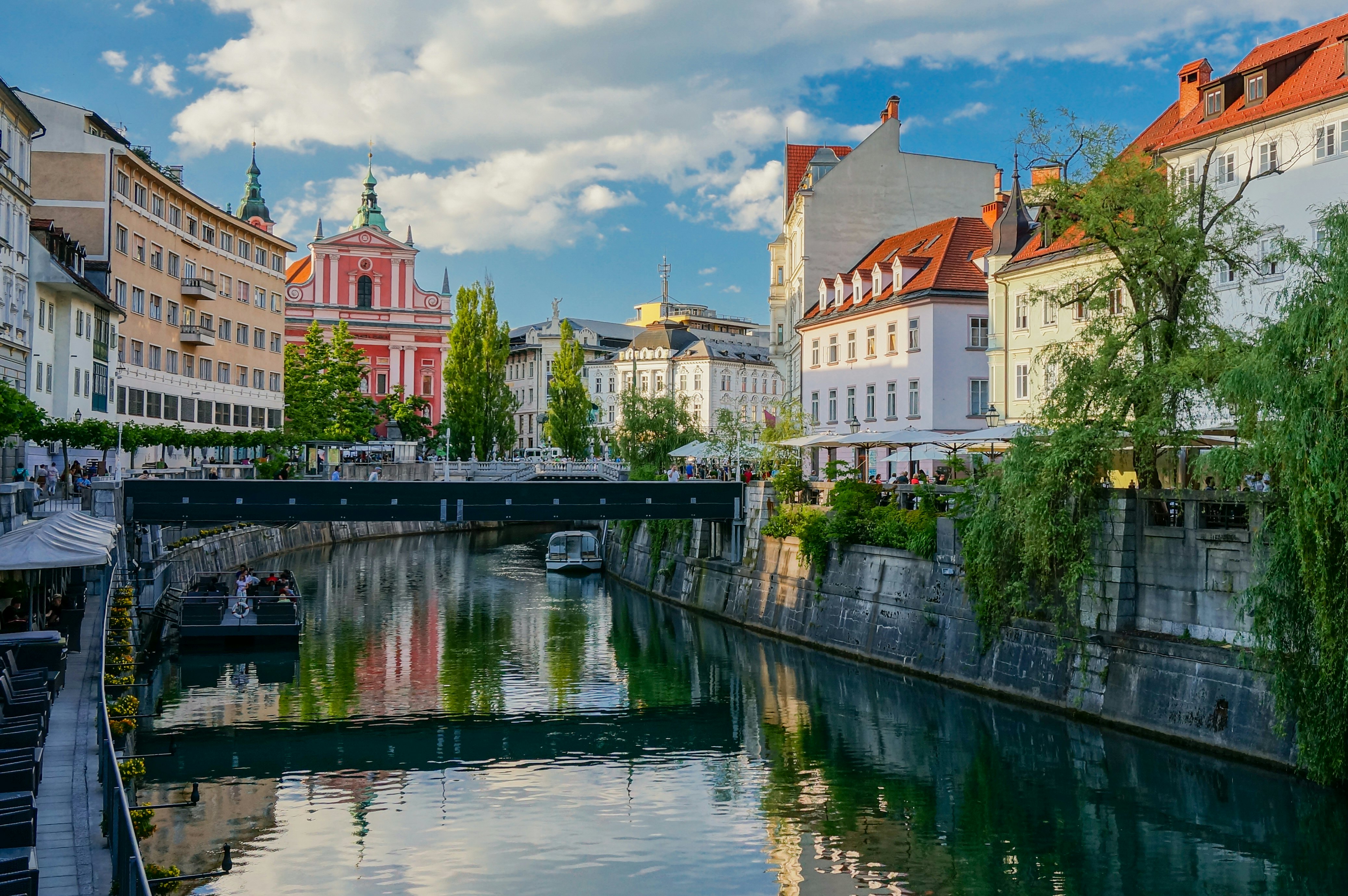 A river runs through a city center passing a church with a pink-hued facade