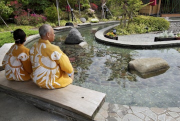 Elderly couple in kimonos dipping feet in ornamental foot bath, Oedo Onsen Monotogari, Odaiba.