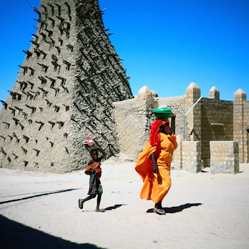 A woman in yellow robes, and a child walk past the Sankore mosque, built in the traditional Sahel style, Timbuktu.