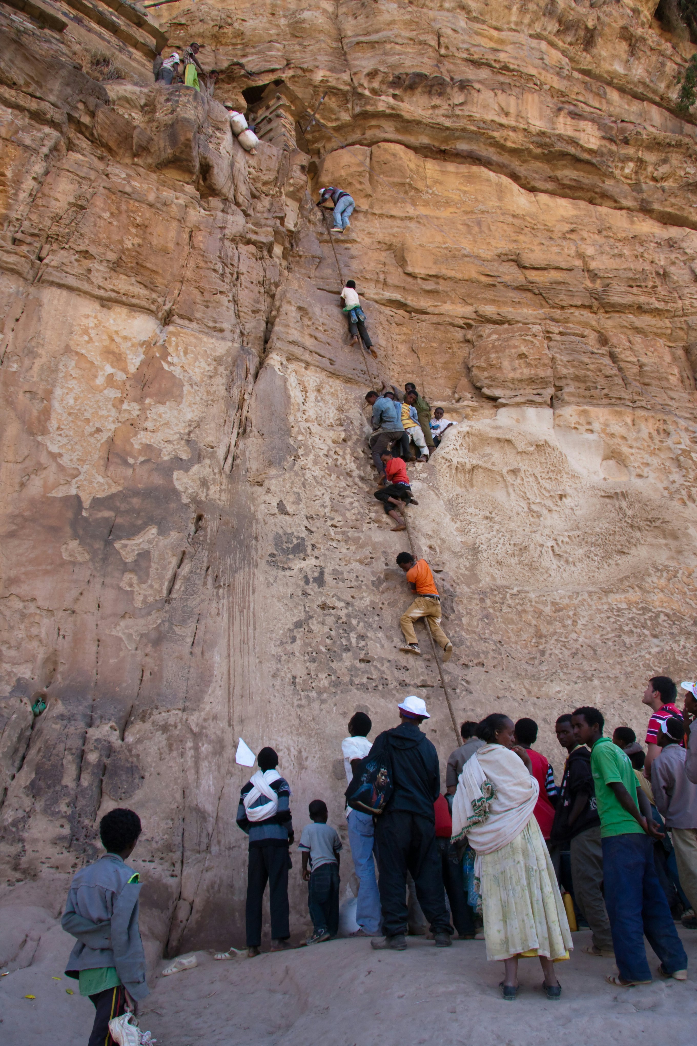 Orthodox Christian pilgrim men being hauled up a 15m cliff face by monks to reach the mountain-top church and monastery of Debre Damo, Northern Tigray province, Ethiopia.