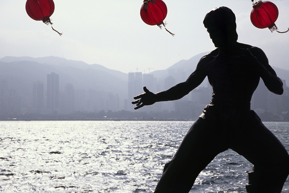 China, Hong Kong, Kowloon. A statue of Cult figure Bruce Lee is silhouetted on the Hong Kong waterfront. The Avenue of the Stars on the Tsim Sha Tsui East Promenade pays homage to the stars of the Hong Kong film industry.
