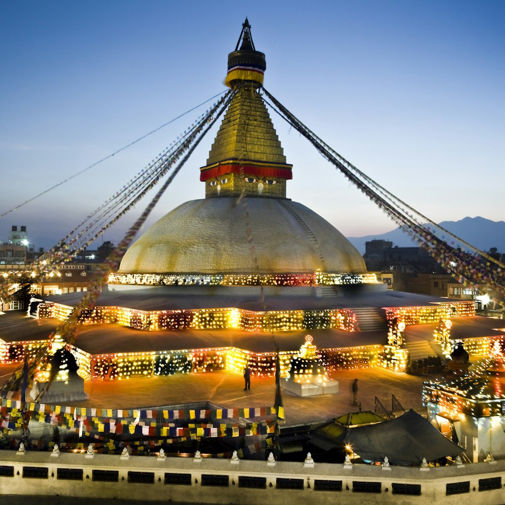 Nepal, Kathmandu Valley, Bodhnath Stupa, the Buddha's eyes and prayer flags viewed at twilight with decorative lights