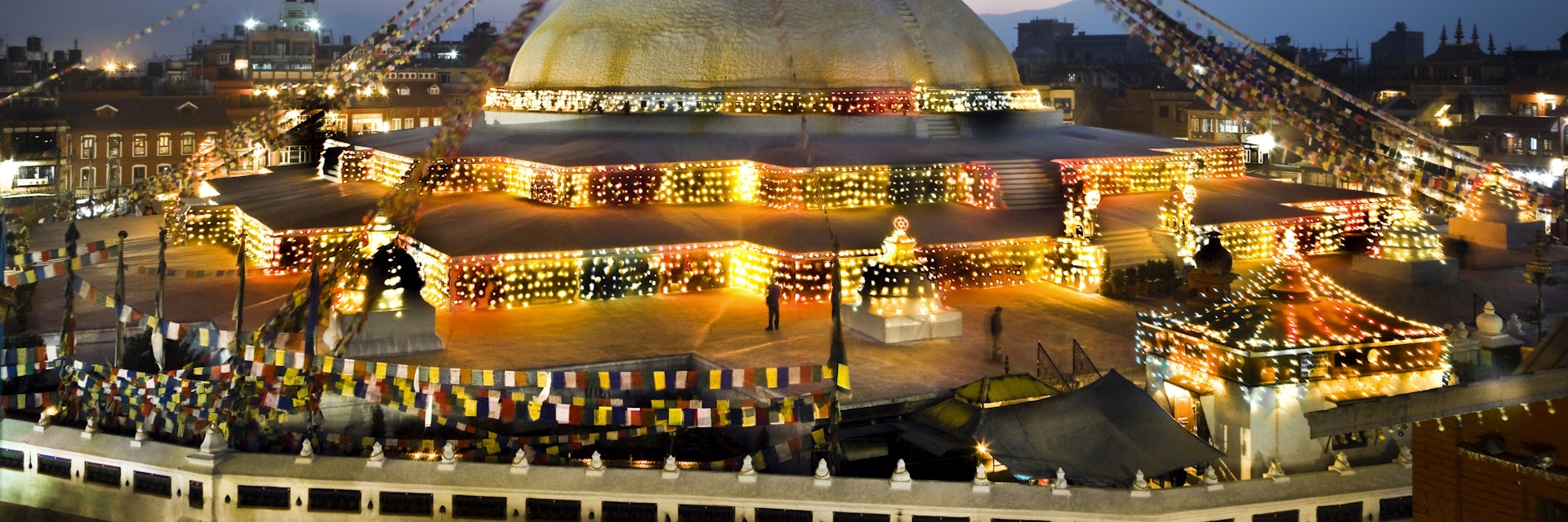 Nepal, Kathmandu Valley, Bodhnath Stupa, the Buddha's eyes and prayer flags viewed at twilight with decorative lights