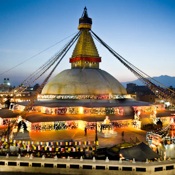 Nepal, Kathmandu Valley, Bodhnath Stupa, the Buddha's eyes and prayer flags viewed at twilight with decorative lights