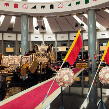 Interior of ther Royal Regalia Museum with sultan's gilded coronation cart and shields.