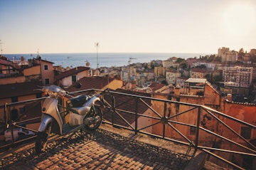 Scooter left on top of "La Pigna" - old town of Sanremo, Italy. View of Sanremo's old and new buildings and Mediterranean sea in the evening.