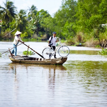 Boy using boat to transport bicycle across river.