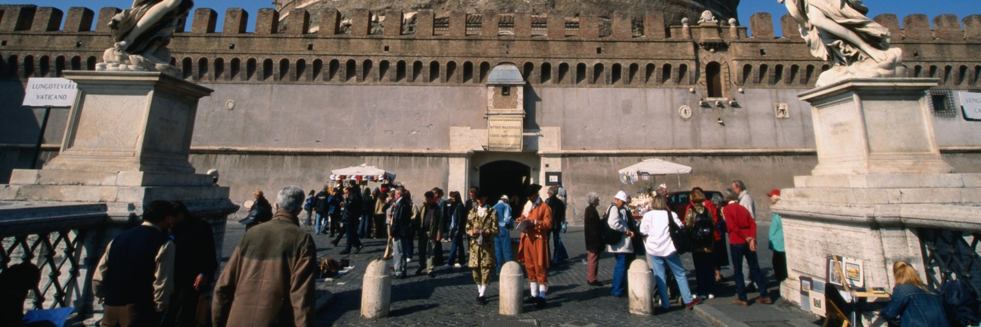 Tourists on the Pont Sant'Angelo make their way past the angels by Bernini and his pupils through to the heavily fortified Castel Sant'Angelo, Rome.