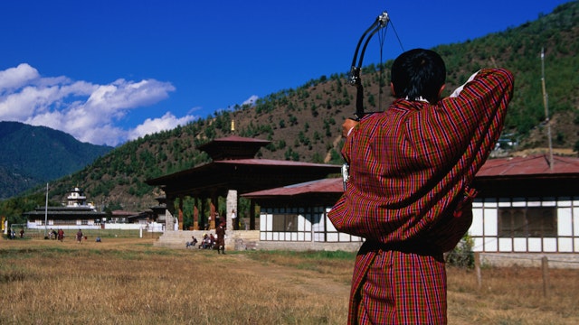 Archer in traditional dress drawing bow in archery competition at national archery ground, Changlimithang Stadium.