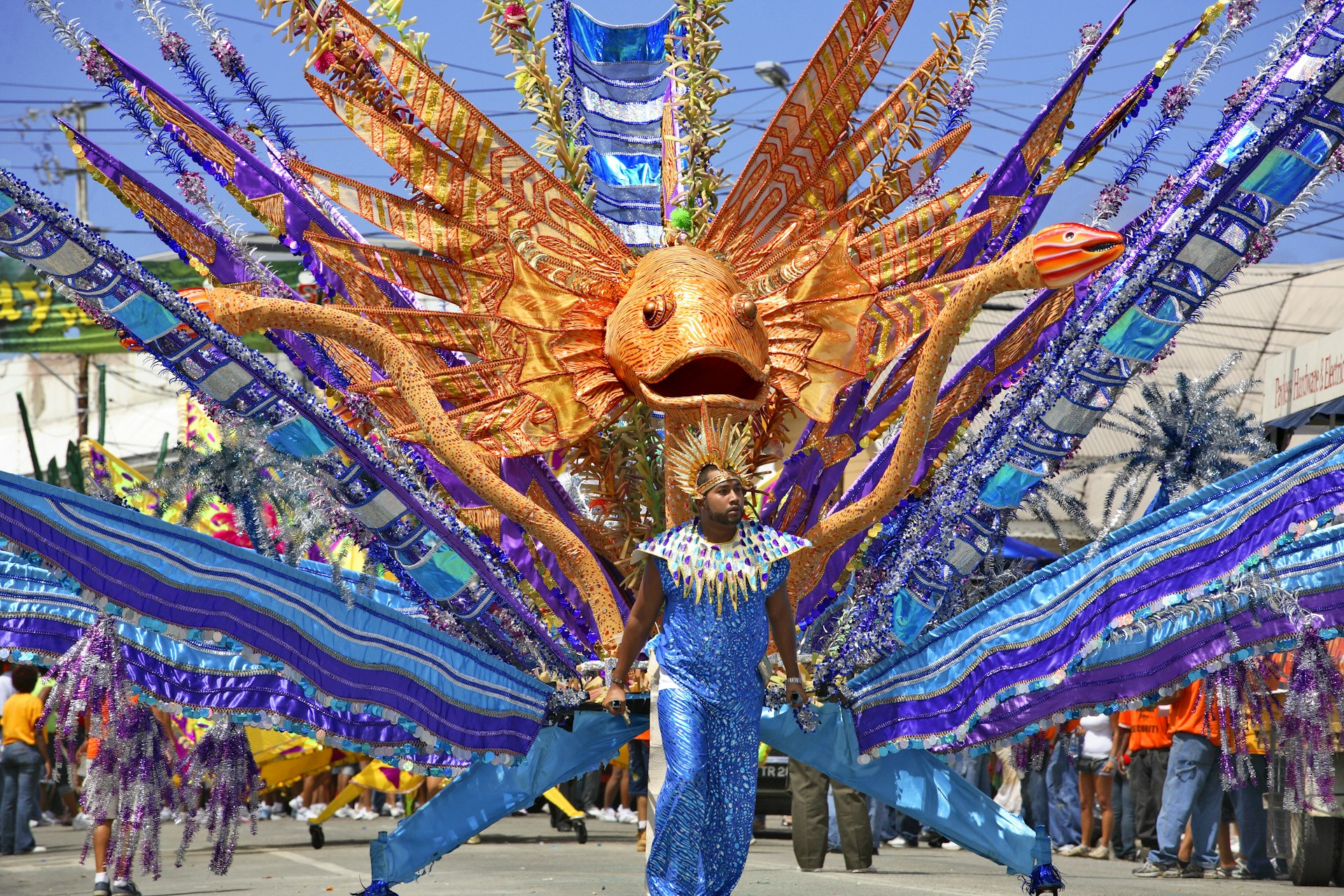 A costumed man in a Carnival parade in front of a giant fish float