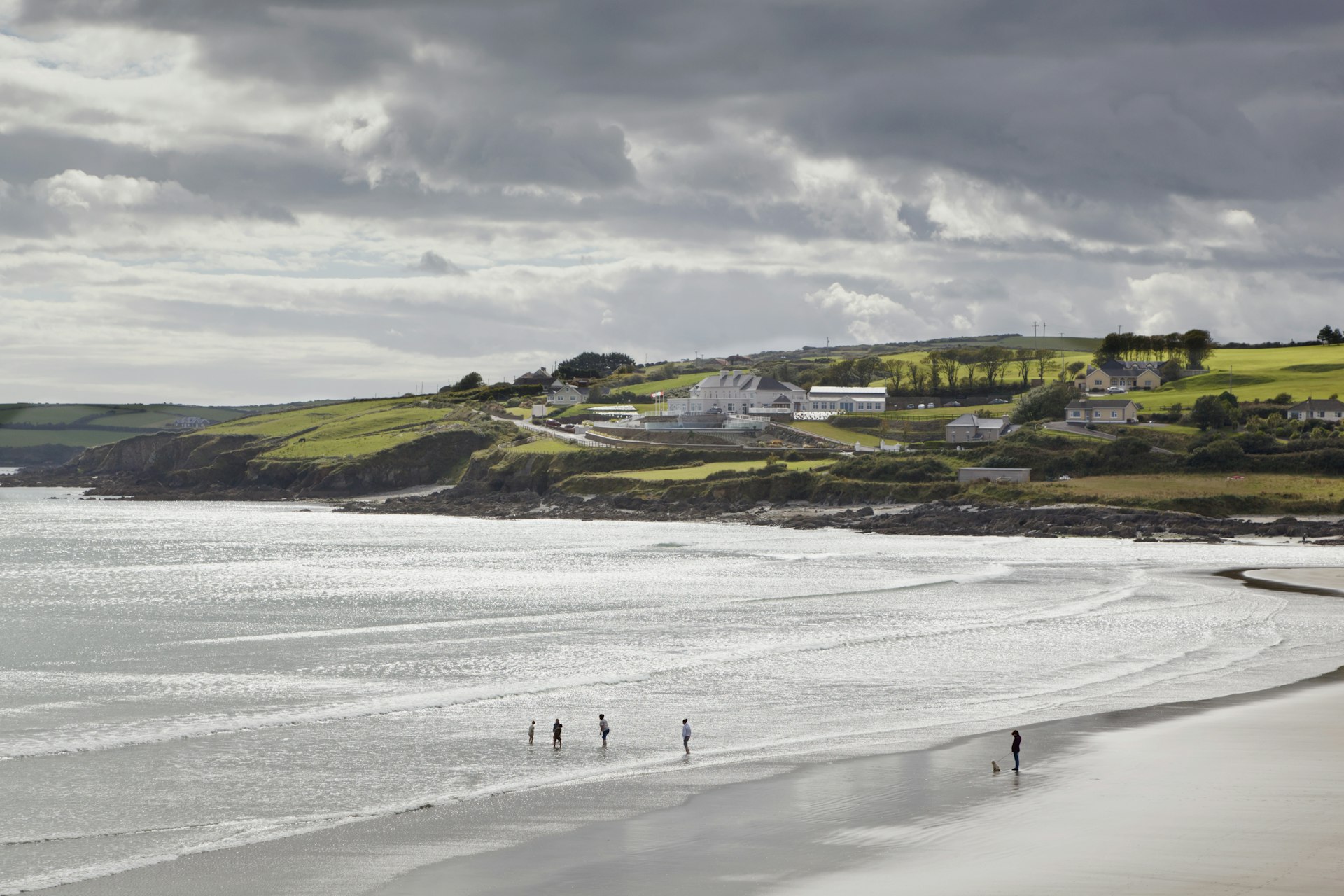 People walk along an Irish beach with lush greenery in the background. 