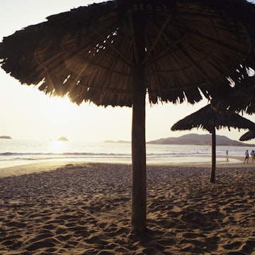 Mexico, Ixtapa, ocean sunset with couples walking along shoreline, umbrellas in sand.