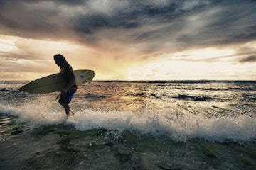 Surfer exiting water with surfboard at sunset in Rincon, Puerto Rico