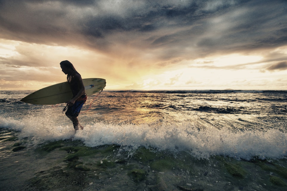 Surfer exiting water with surfboard at sunset in Rincon, Puerto Rico