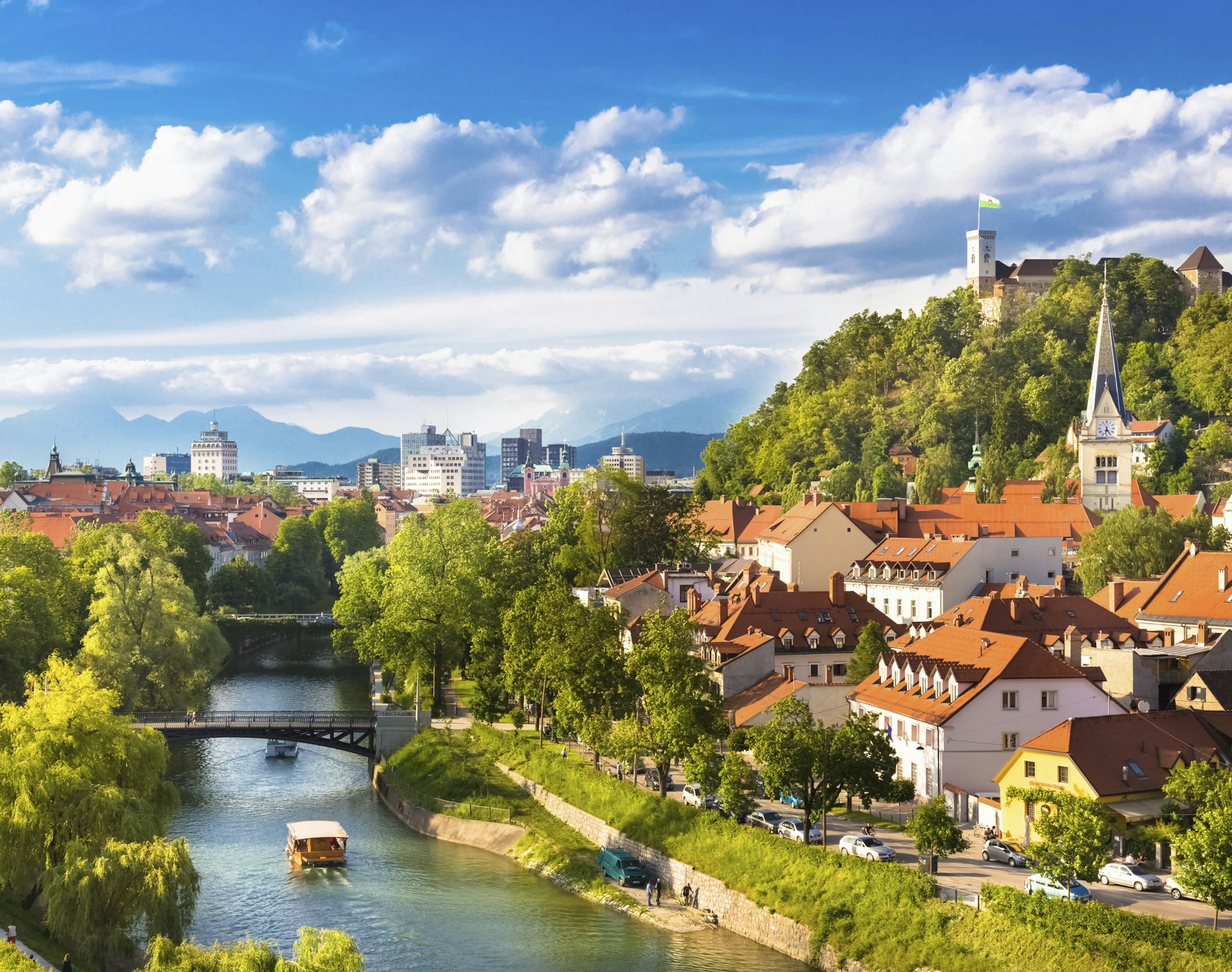 A panorama of Ljubljana, with a river, lush hills, and buildings with terracotta-colored roofs