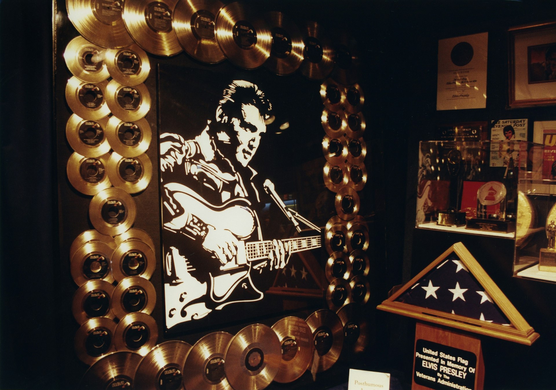 Gold records serve a frame for a black-and-white portrait of Elvis Presley, plus a folded American flag and other memorabilia at Graceland