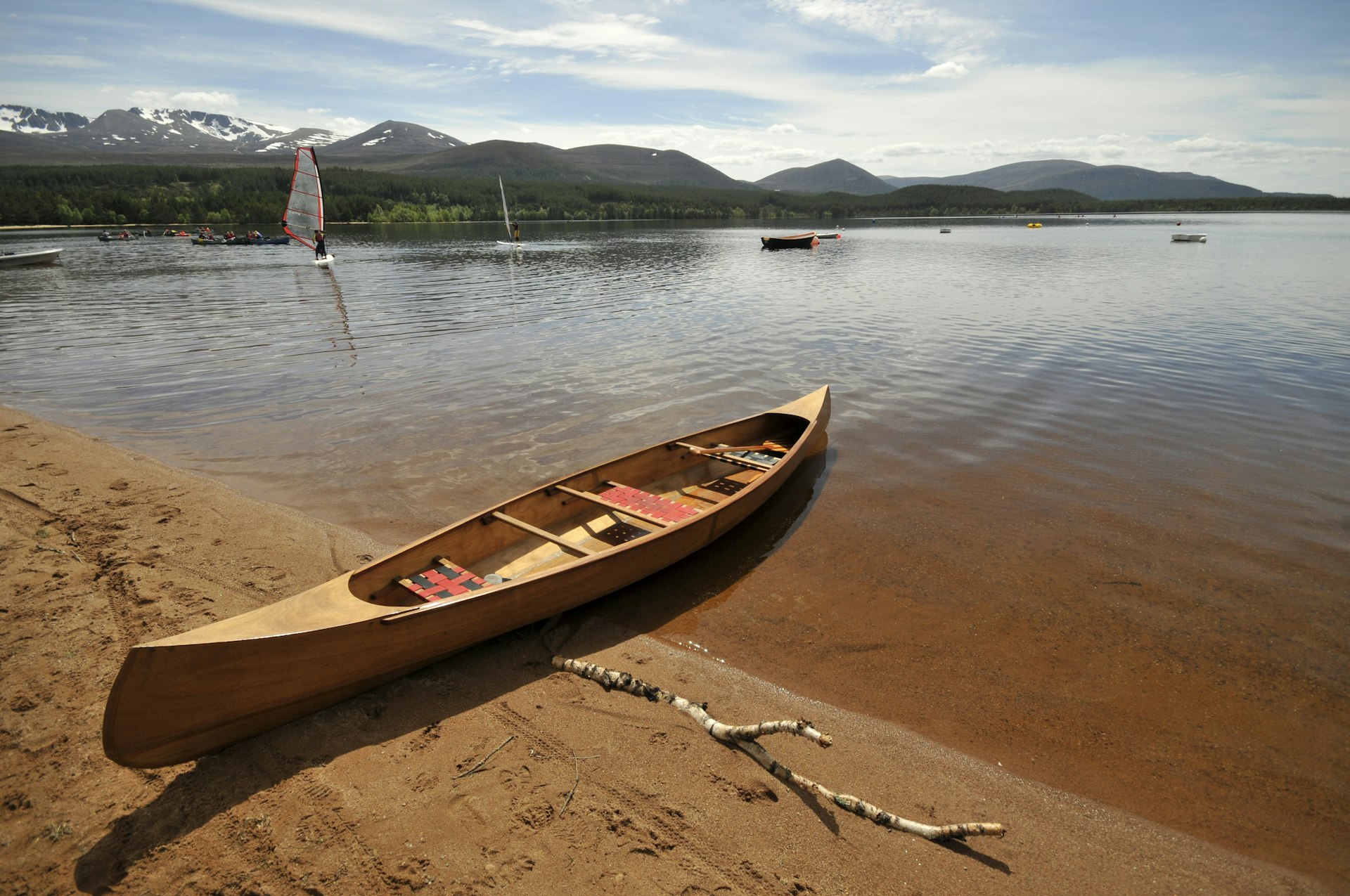 A canoe on the beach and windsurfer on the water of Loch Morlich, National Park of Cairgorns, Scotland, United Kingdom