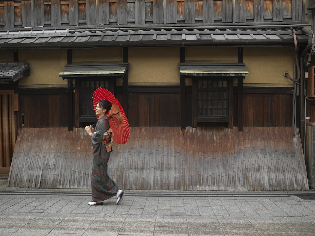 Japan, Kyoto, Gion, woman in kimono with red oilpaper umbrella, walking in street